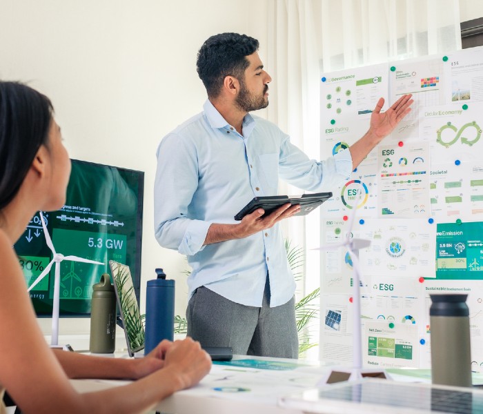 Man in office stood in front of a presentation board. On the board are reports about ESG.