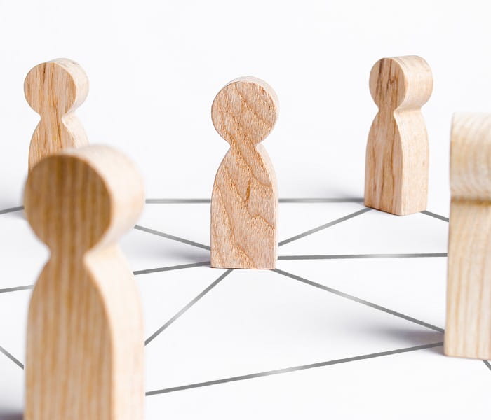 Seven wooden statues interlinked by a network of grey lines, representing collaboration and communication.